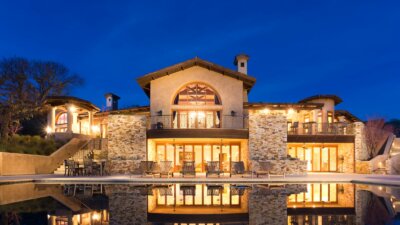 An exterior night photo of the two story house and pool on 16 Vasquez Trail at the Santa Lucia Preserve.